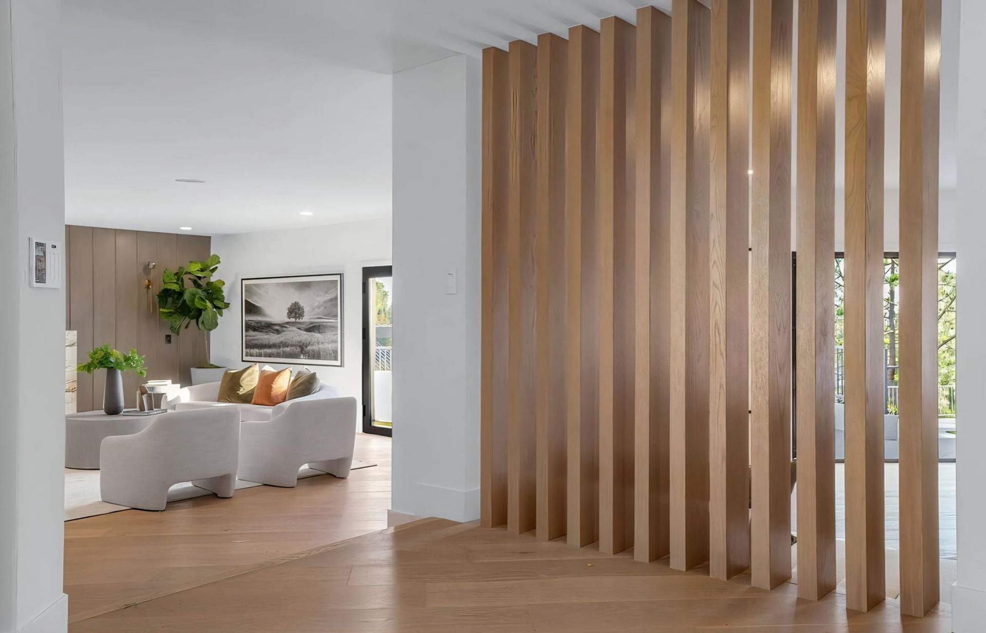 Modern living room with white sofas and a wooden slatted divider in a bright open-plan home