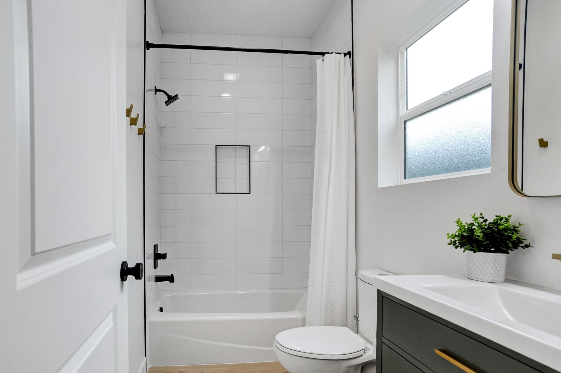 Bright bathroom with a bathtub, white tile, window, and vanity sink.
