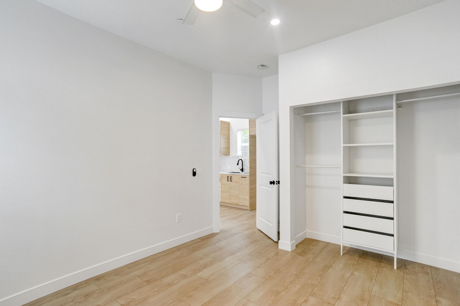 Empty white bedroom with wood floors and an open closet beside the doorway.