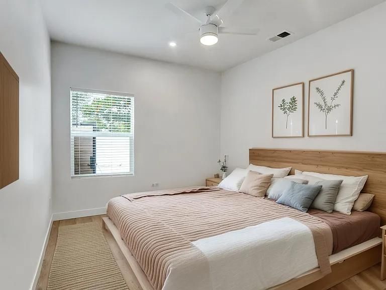 Bright bedroom with a king bed, white walls, framed art, window, and ceiling fan
