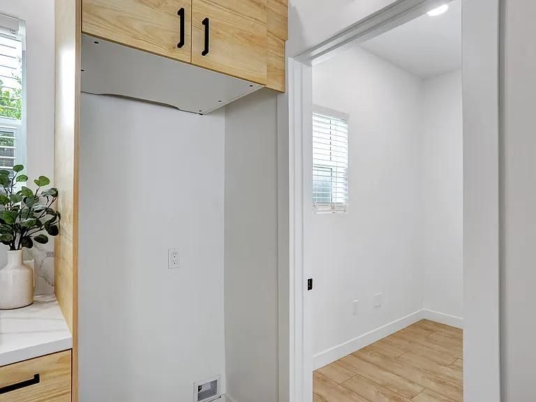 Bright hallway with wood cabinets, a countertop, and an open doorway to a white room with wood flooring.