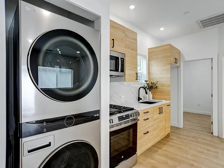 Modern kitchen with stacked washer-dryer, wood cabinets, white countertops, and stainless appliances