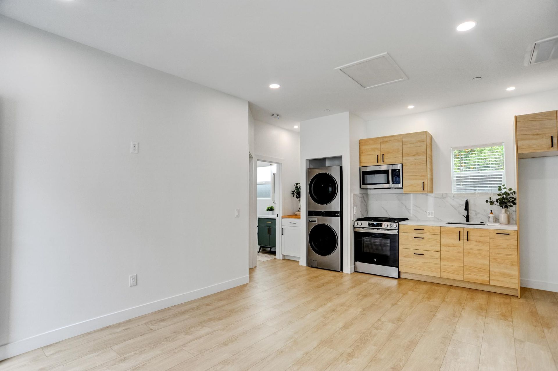 Bright empty apartment kitchen with stacked washer and dryer, wood cabinets, and light wood flooring