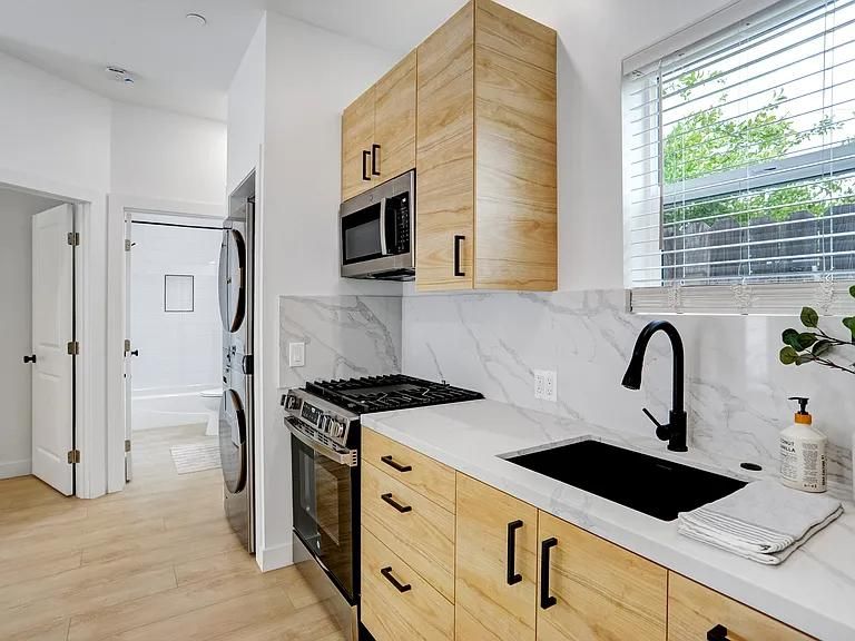 Bright modern kitchen with white cabinets, wood accents, black fixtures, and a large window