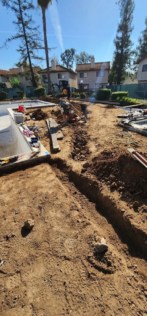 Backyard excavation with trenching, dirt piles, and scattered construction materials near a house