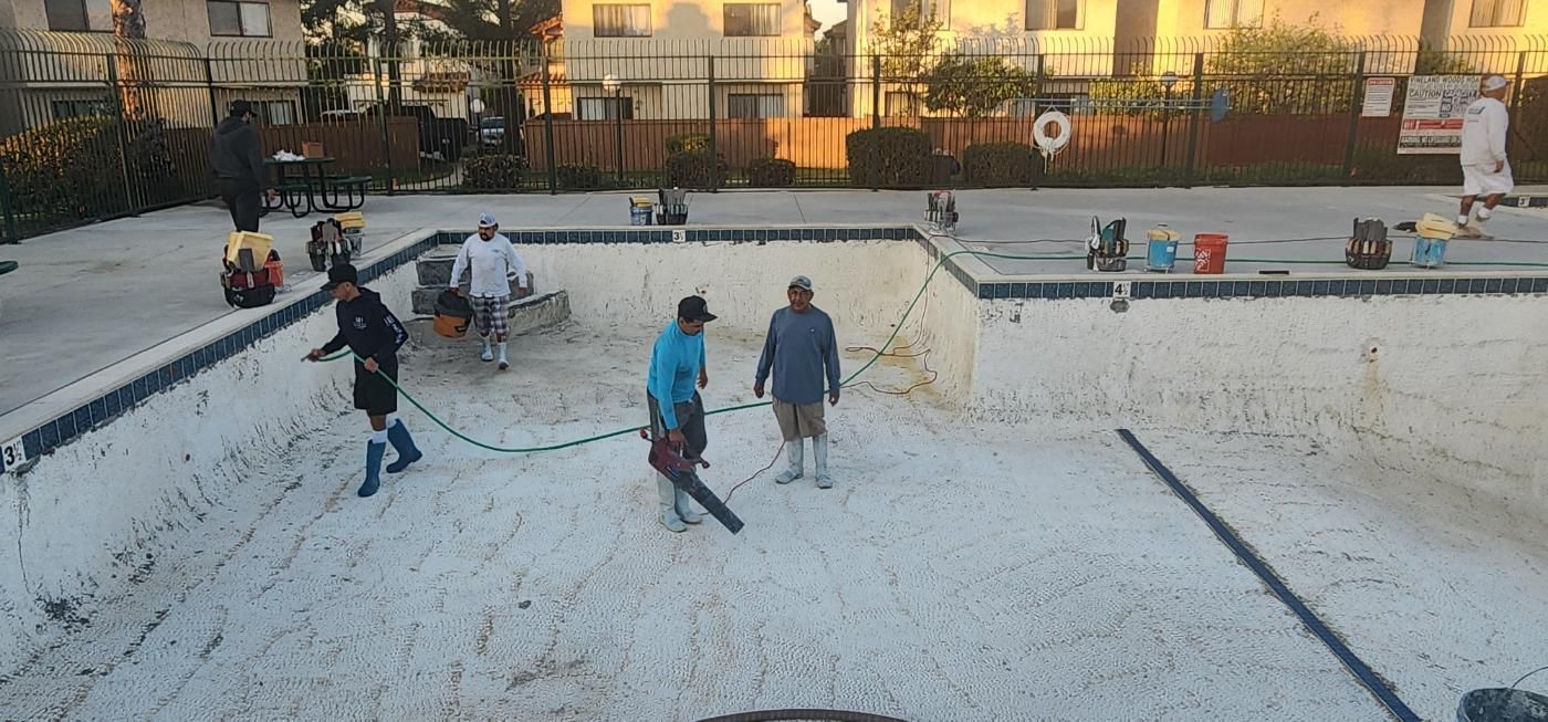 People in a white drained pool, some walking and standing with skateboards at sunset.