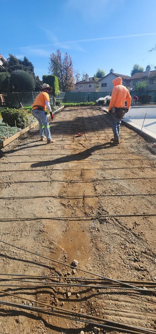 Two construction workers in orange vests leveling dirt on a road under repair