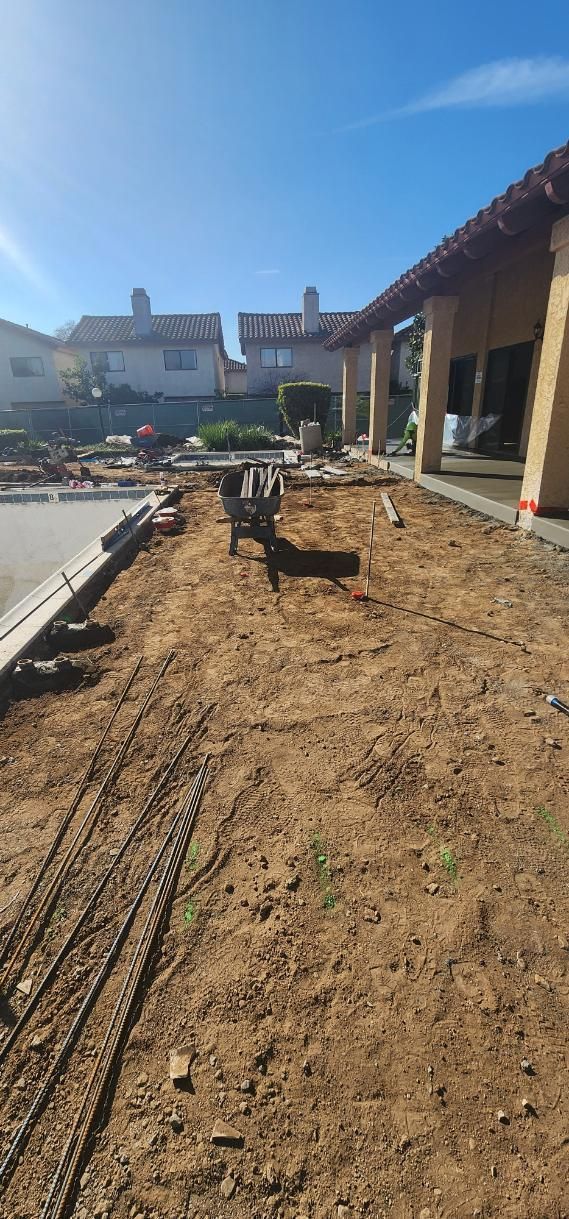 Backyard under construction with wooden framing, dirt ground, and a house porch on the right