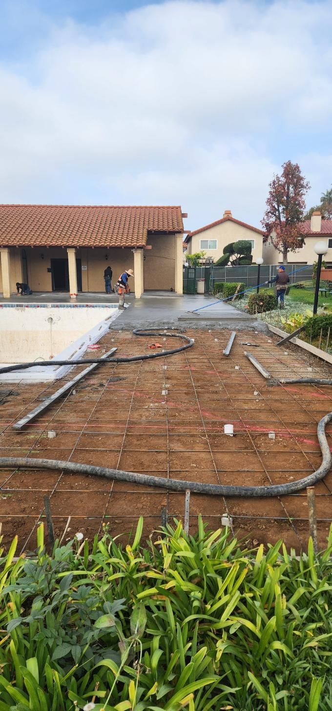 Backyard under construction beside a house, with soil, pipes, and a concrete walkway.
