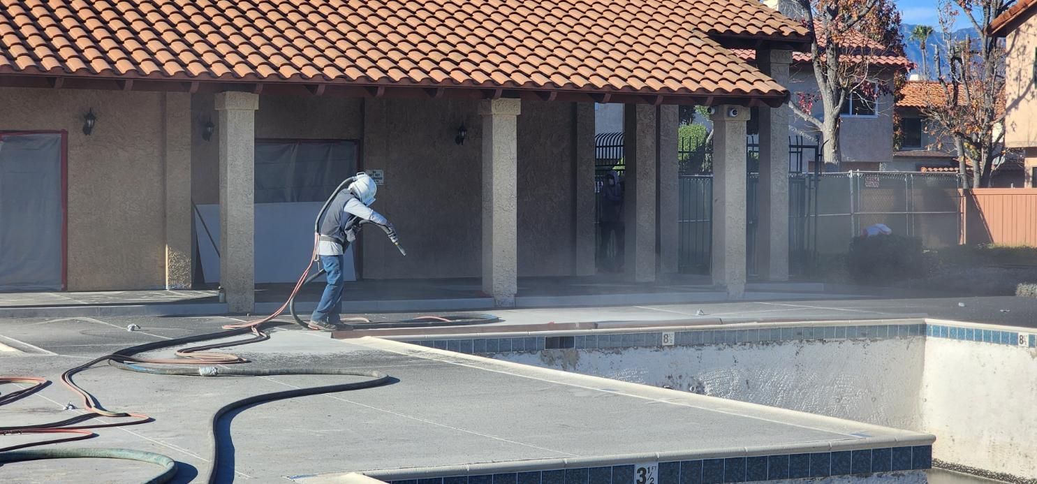 Worker using a pressure washer on a concrete pool deck beside a house