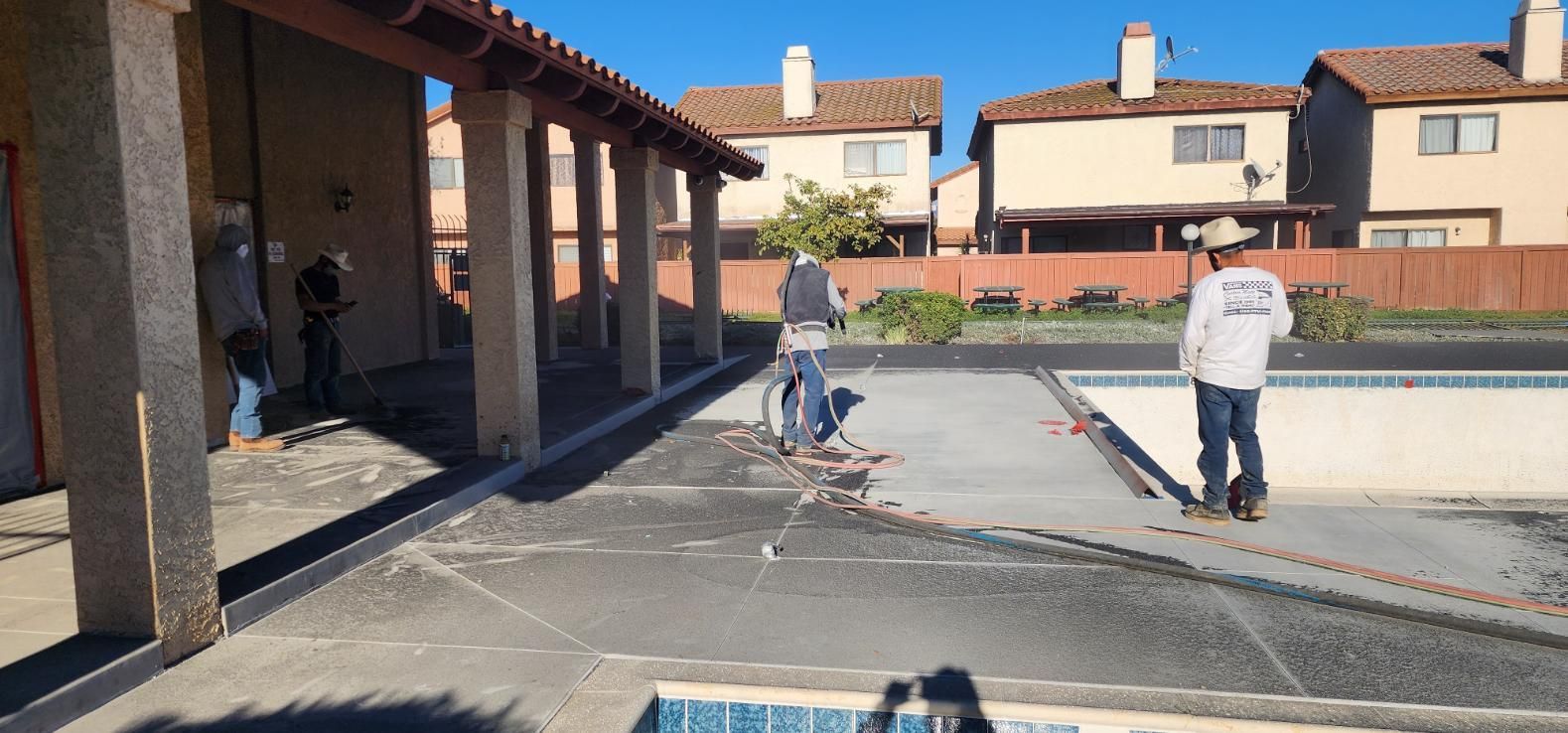 Two workers paving a courtyard beside stucco townhouses on a sunny day