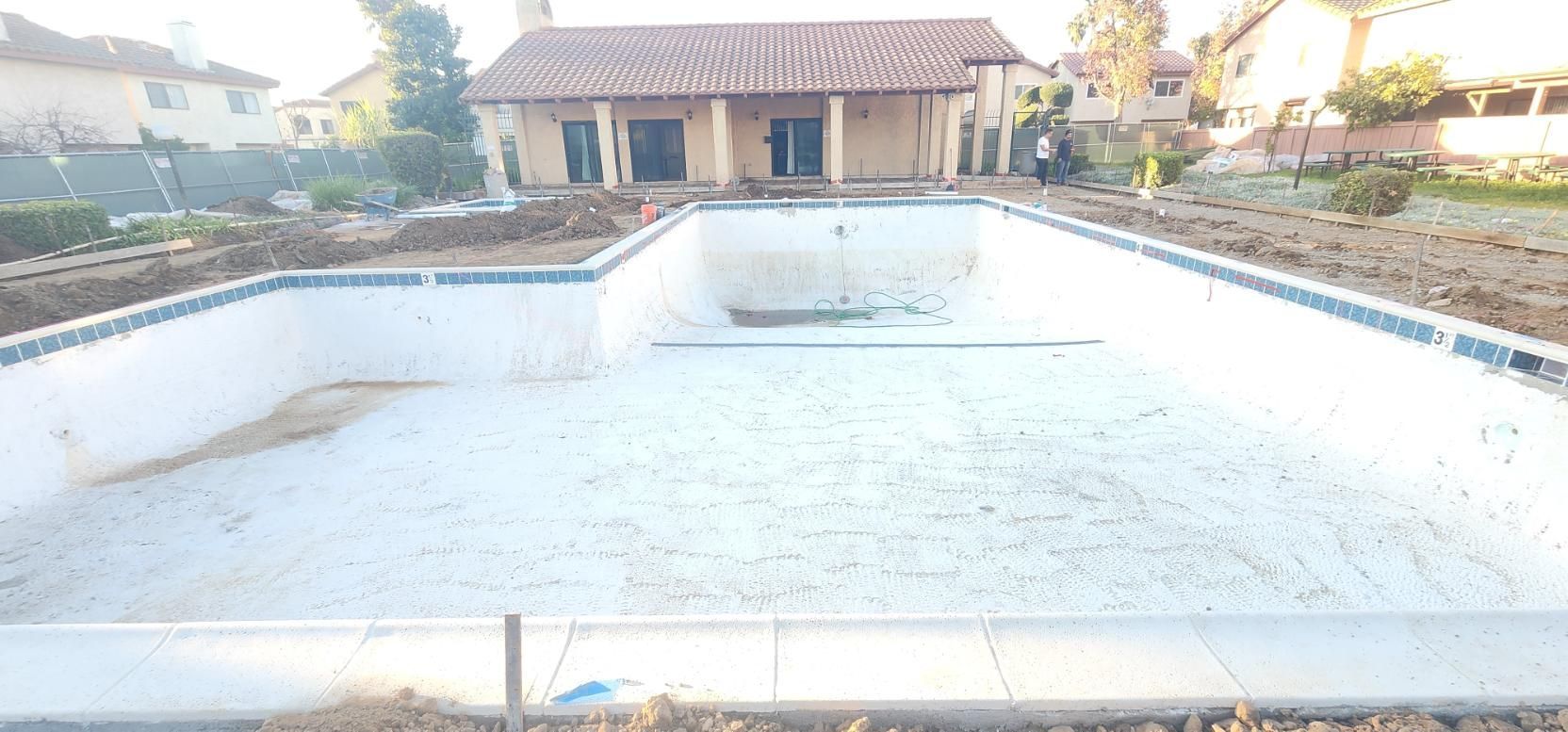 Empty drained swimming pool in a backyard, with a house and garden in the background.