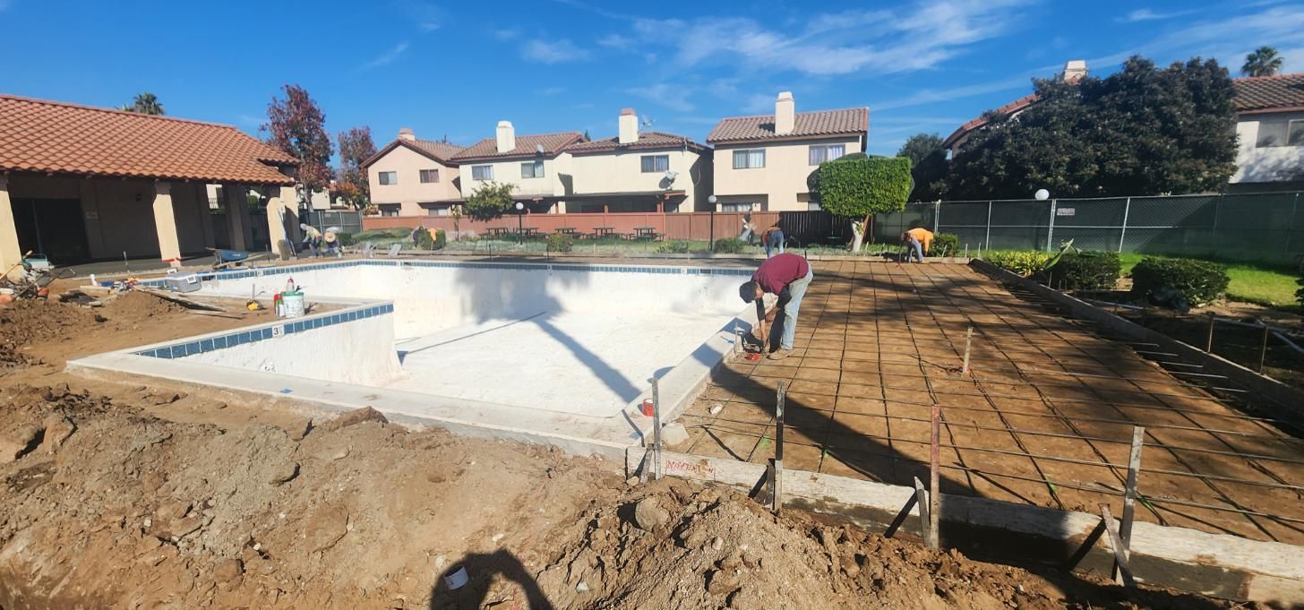 Workers installing concrete around a backyard pool under construction, with houses in the background.