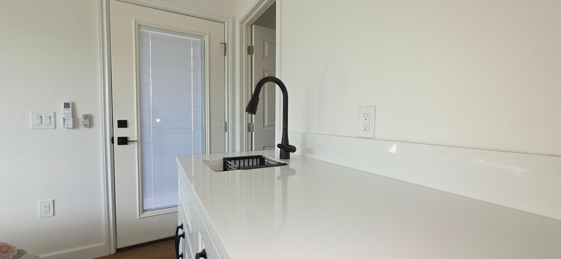 Bright kitchen with white island countertop, black faucet, and a door in the background.