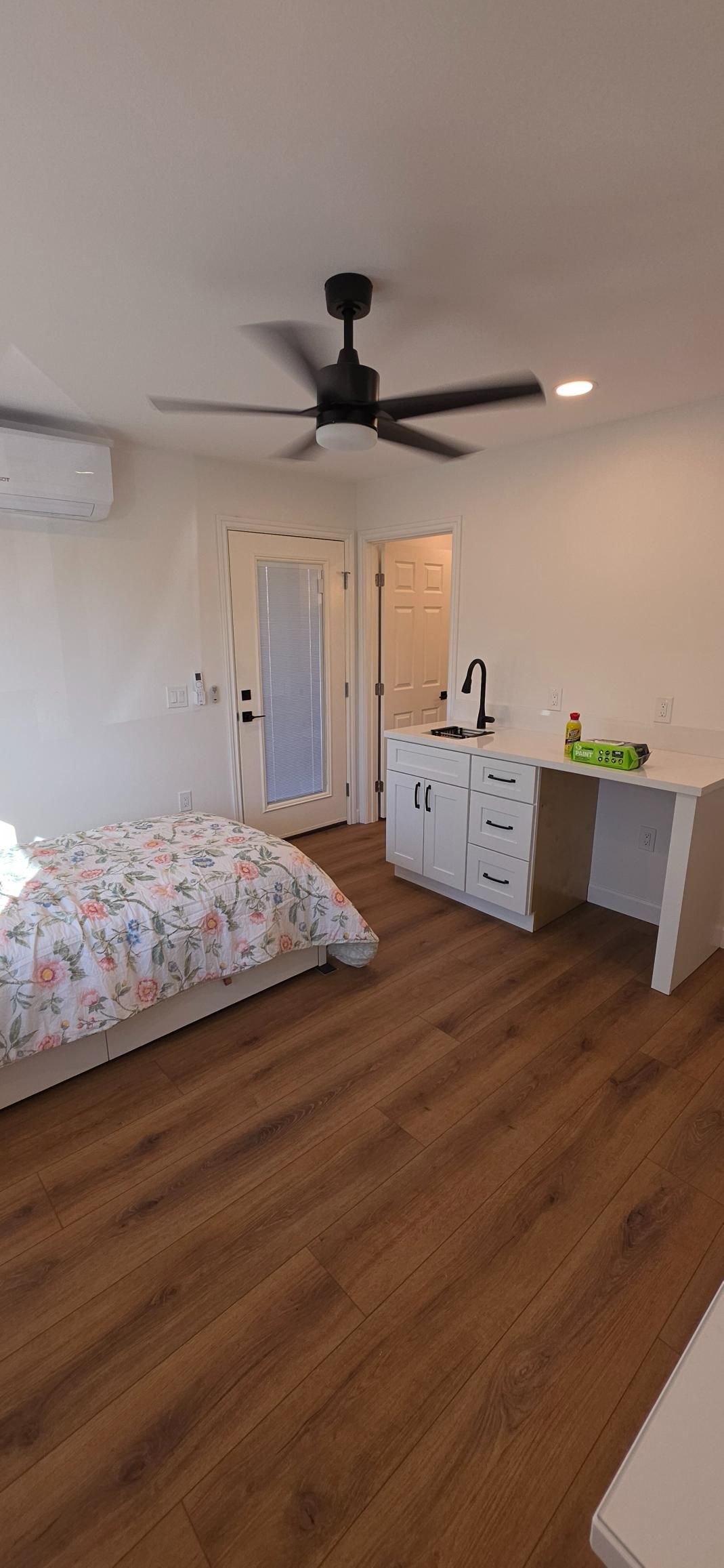 Bedroom with white dresser, bed, ceiling fan, wood floor, and an open doorway to a bathroom