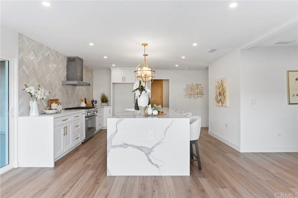 Bright modern kitchen with white marble island, gold pendant light, and stainless appliances