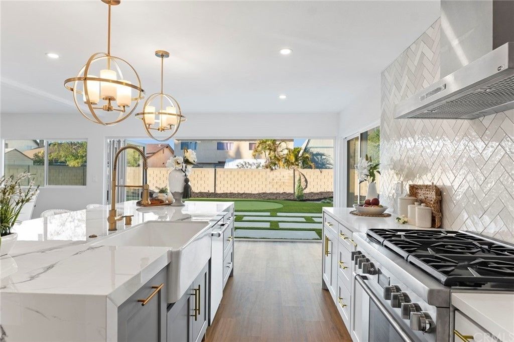 Bright modern kitchen with marble island, brass pendant lights, and open view to a backyard.