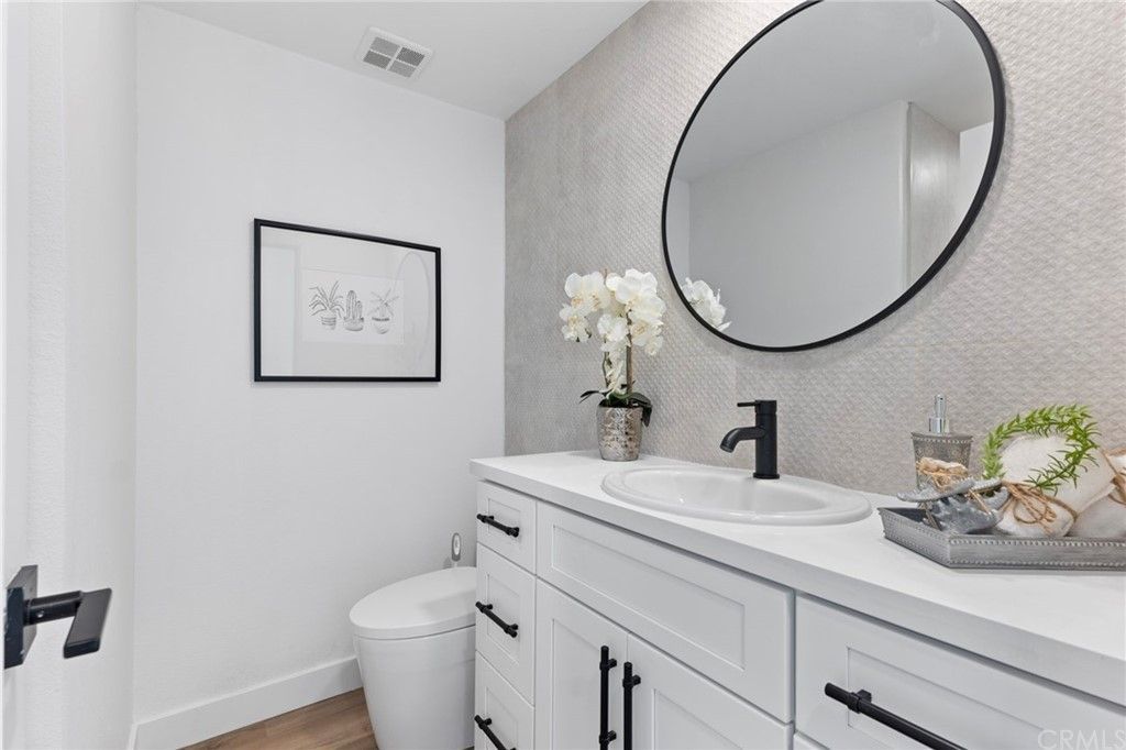 Bright white bathroom vanity with round mirror, black faucet, and framed wall art.