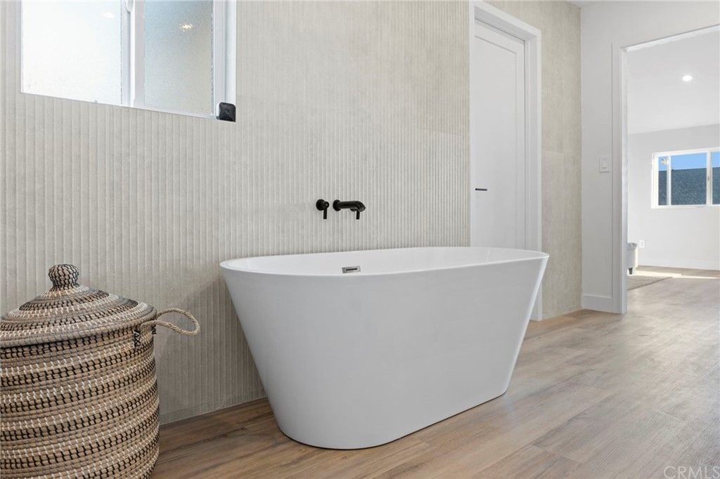 Modern bathroom with a freestanding white tub, woven basket, and light wood flooring