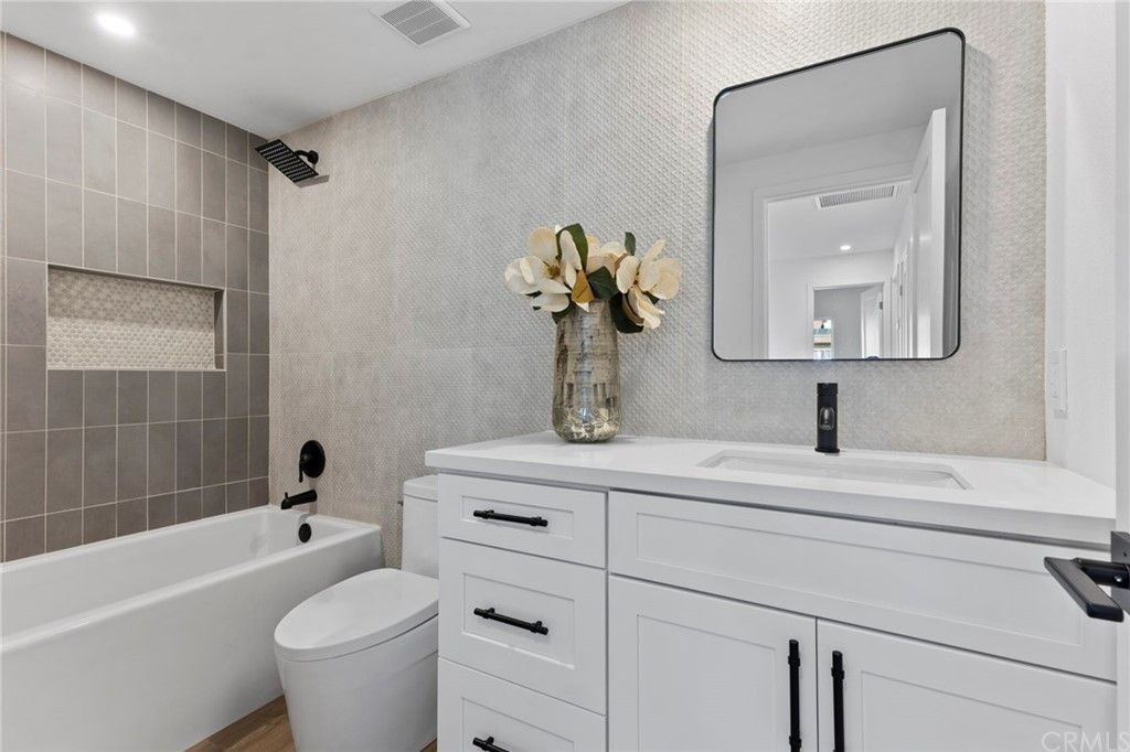 Modern bathroom with white vanity, mirror, tub, and gray tile walls