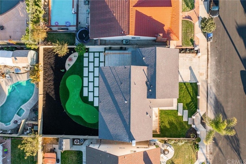 Aerial view of a backyard with pool, putting green, patio, and a house roof beside a street