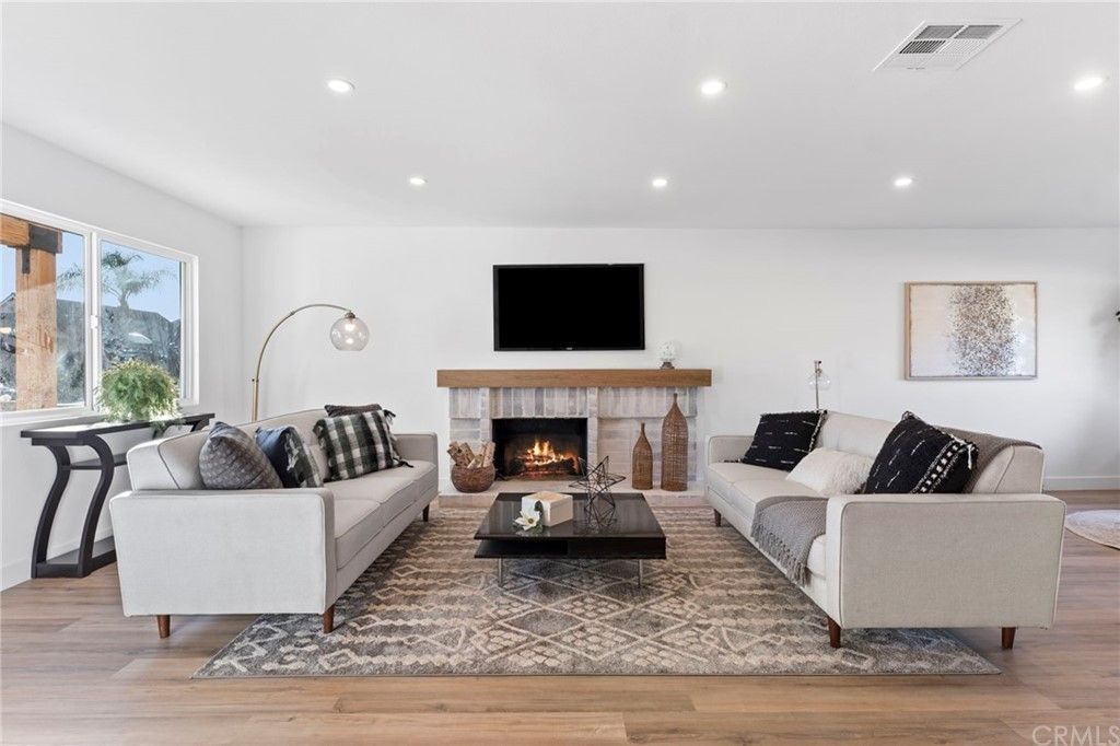 Bright living room with two sofas facing a fireplace and wall-mounted TV, wood floors, and large windows