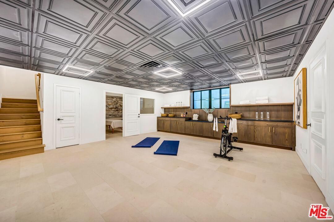 Spacious home gym with patterned ceiling, mirrored wall, exercise bike, and blue mats on beige carpet.
