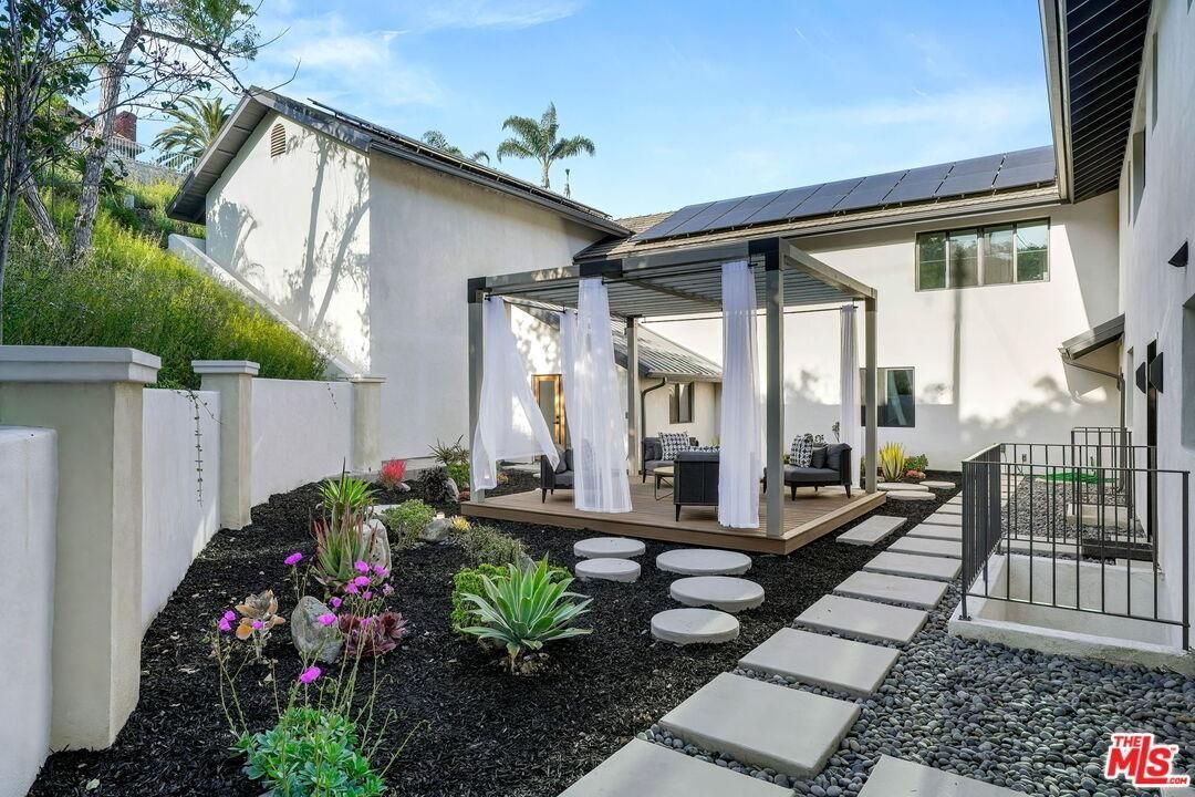 Modern backyard patio with stepping stones, potted plants, and white stucco walls under a blue sky