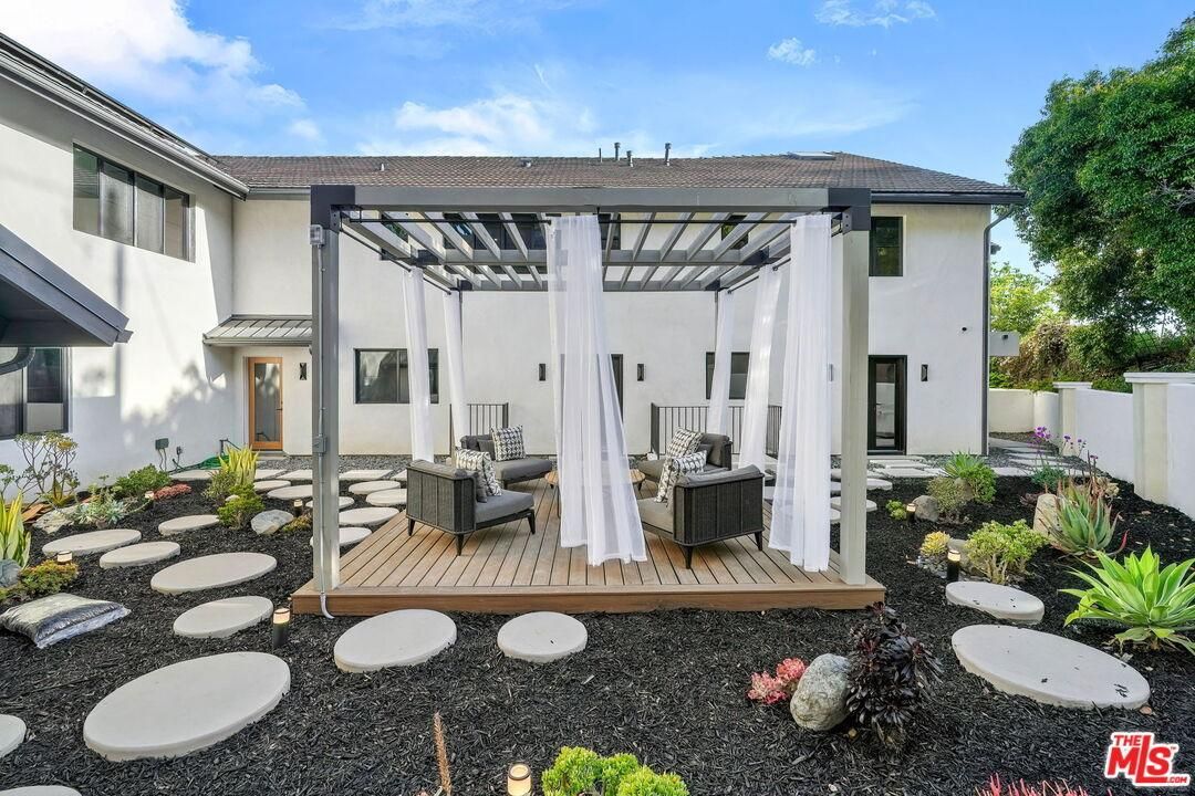 Backyard pergola with white curtains, patio seating, and stepping stones in a landscaped yard