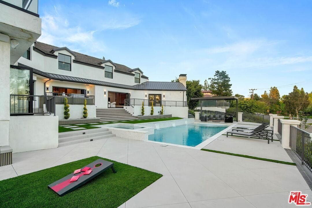 Luxury modern home with a backyard pool, patio lounge chairs, and green lawn under a clear sky