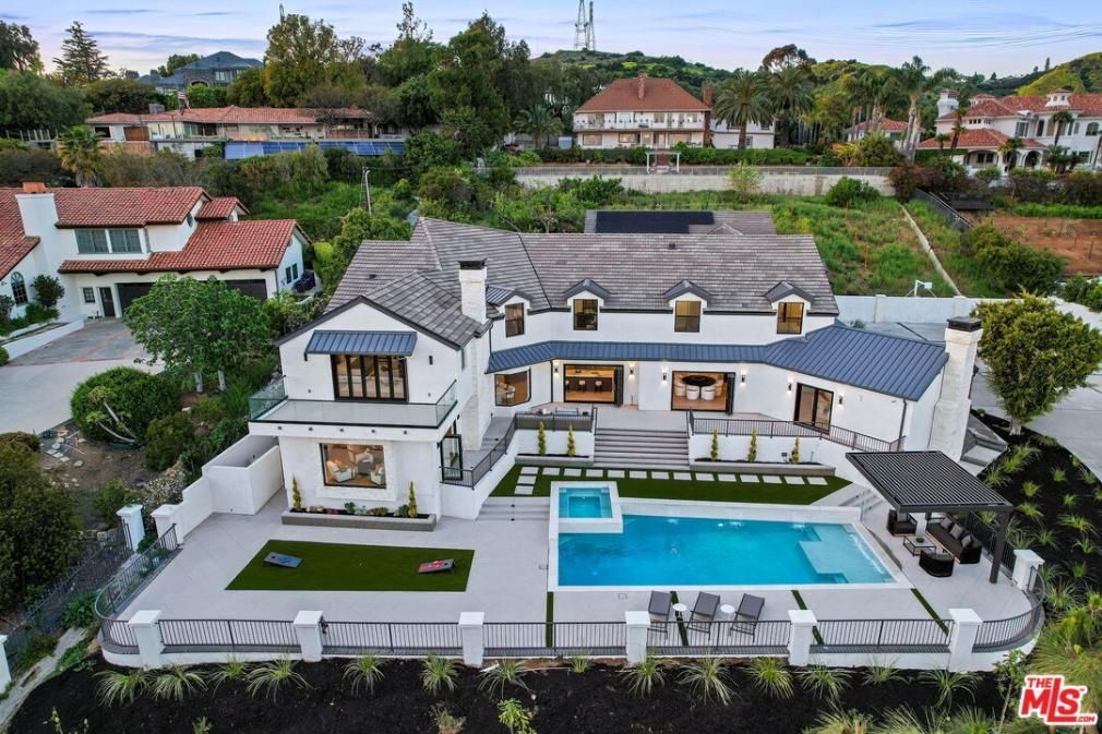 Aerial view of a large white luxury home with a pool, patio, and manicured landscaping.
