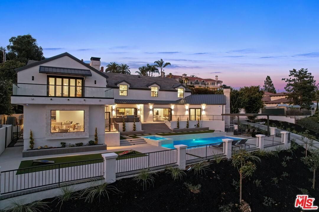Modern hillside mansion at dusk with lit windows, pool, and city view