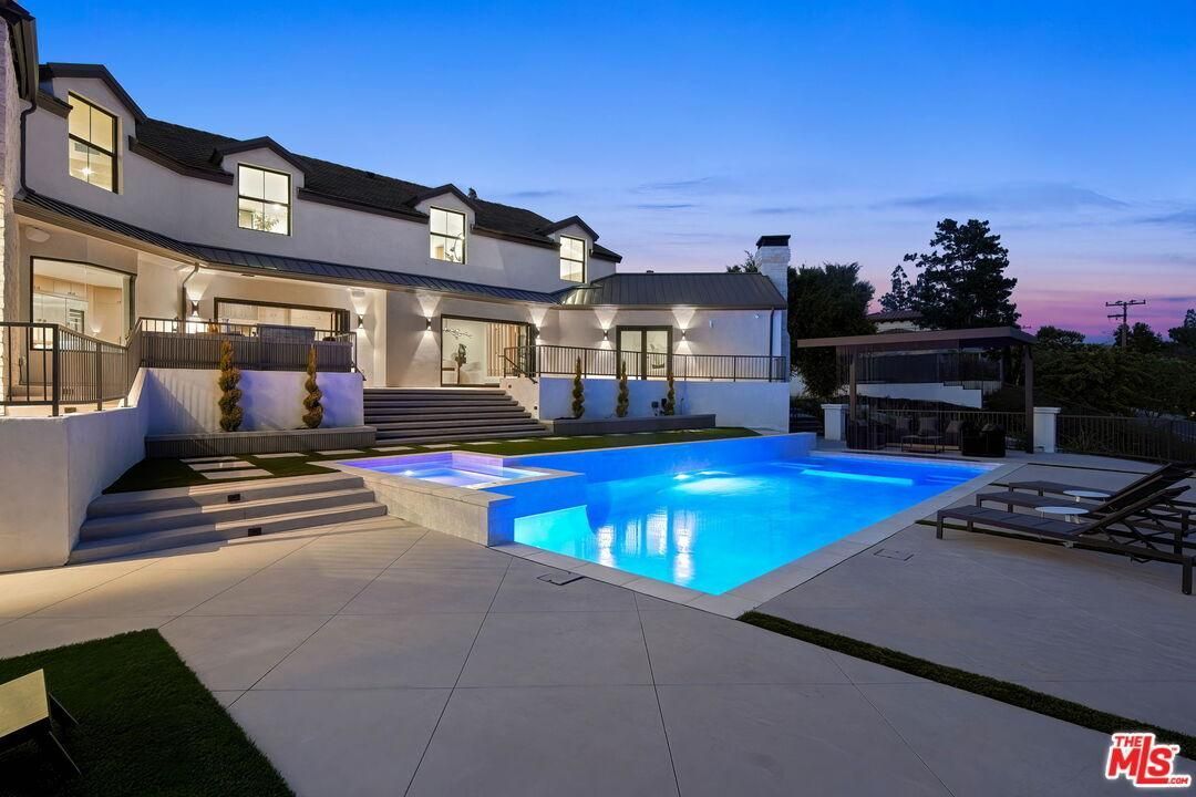 Luxury home with lit backyard pool and patio at dusk
