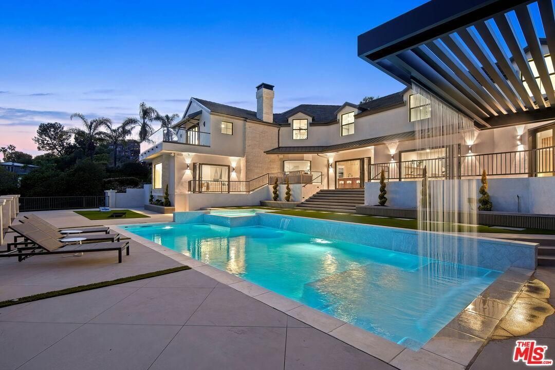 Luxury house with illuminated backyard pool at dusk and modern patio seating