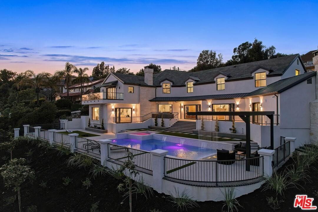 Modern hillside house with glowing pool, terrace, and warm evening lights at sunset