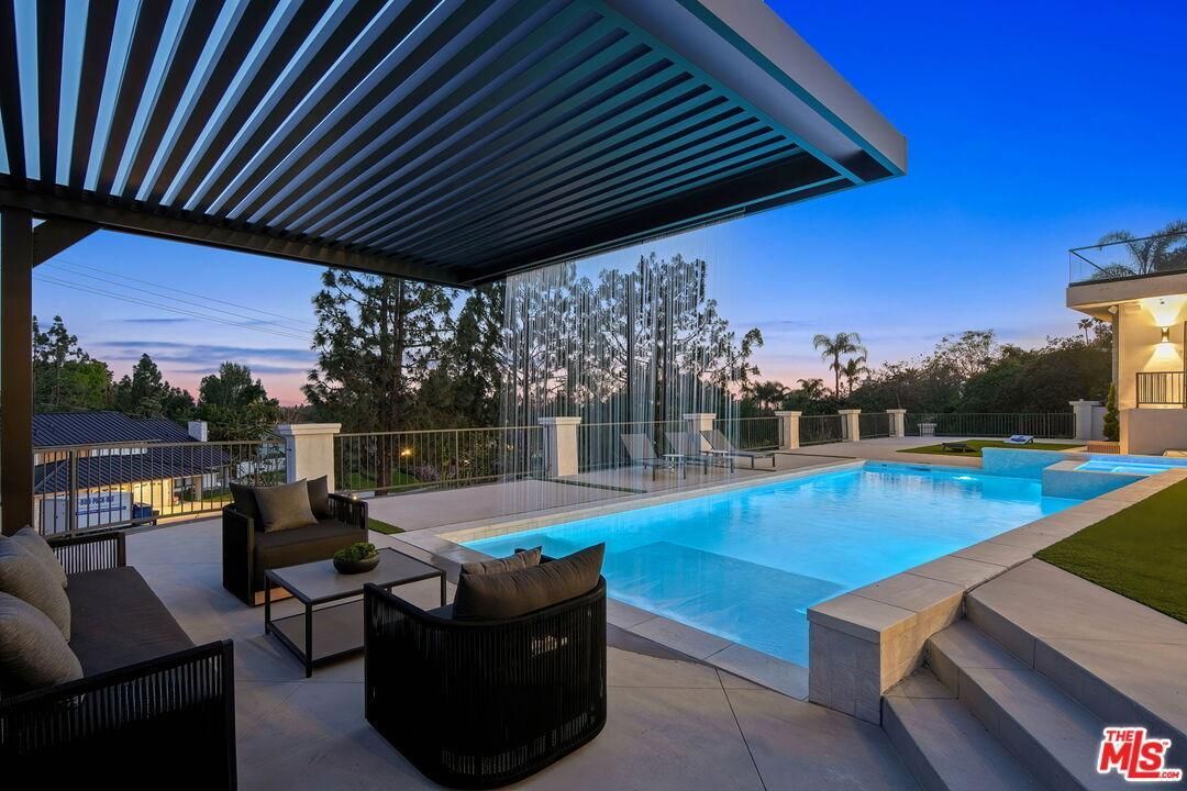Modern backyard pool at dusk with lounge chairs, pergola, and blue water reflecting the sky