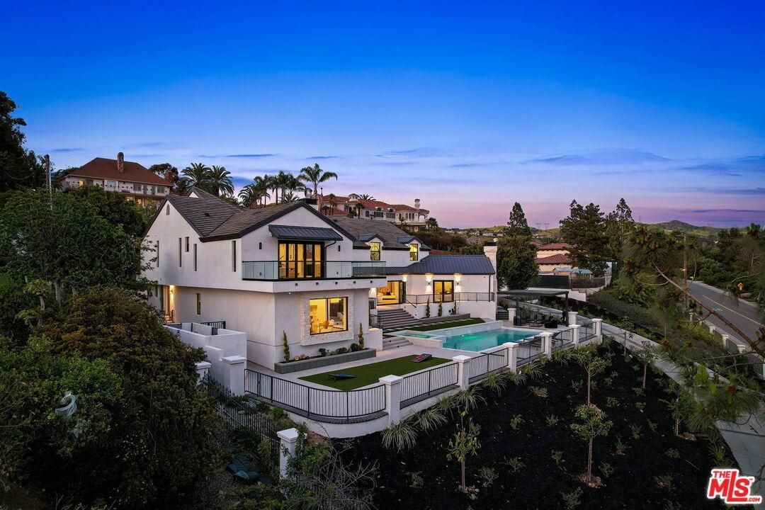 Modern hillside mansion at dusk with lit windows, pool, and city views