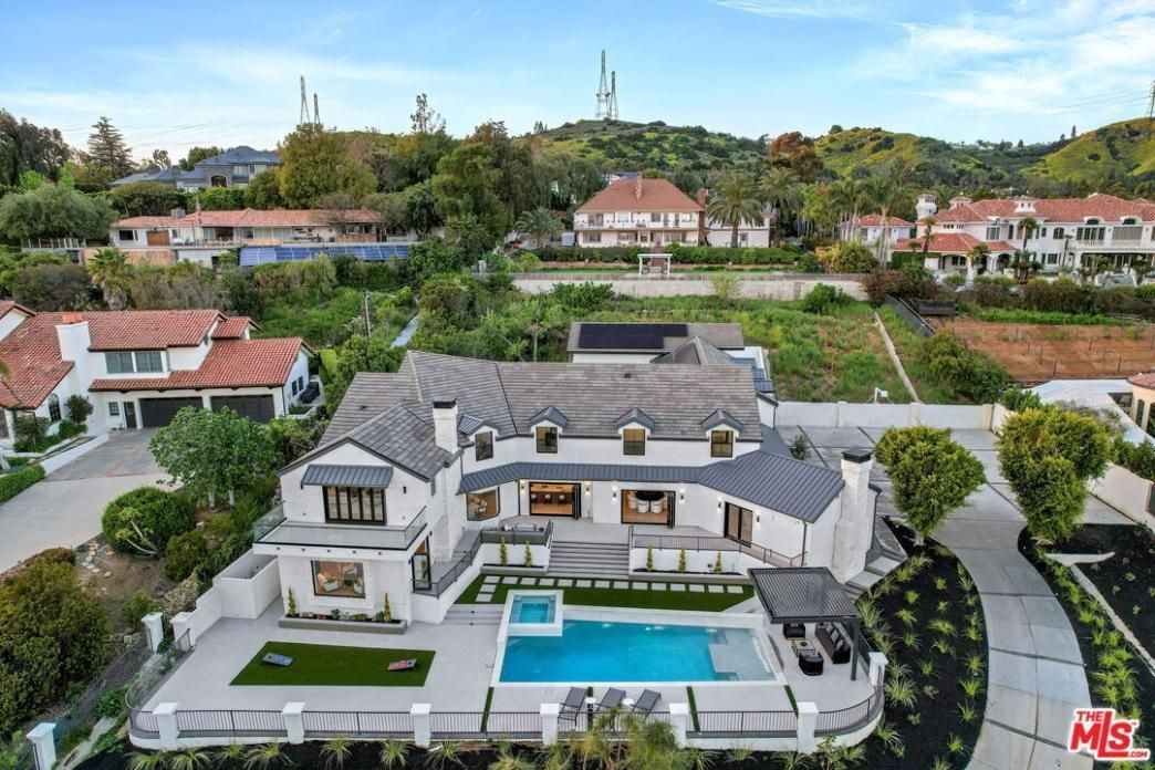 Aerial view of a large modern house with a pool and landscaped yard in a hillside neighborhood