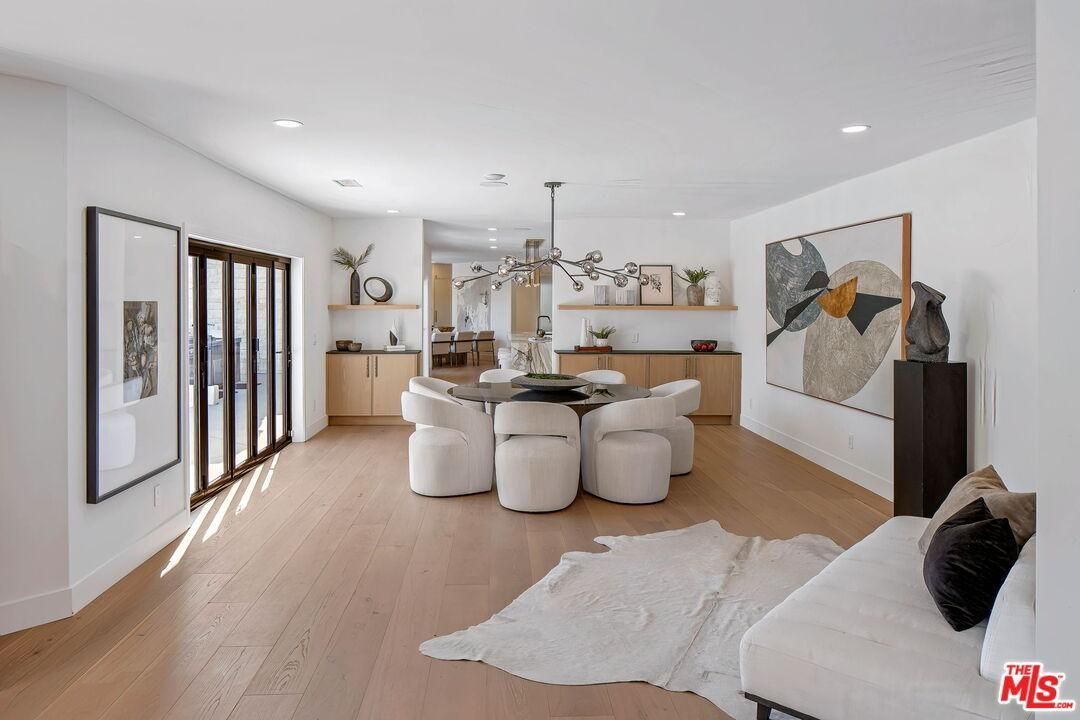 Bright open living room and kitchen with light wood floors, round ottomans, modern art, and a white sofa