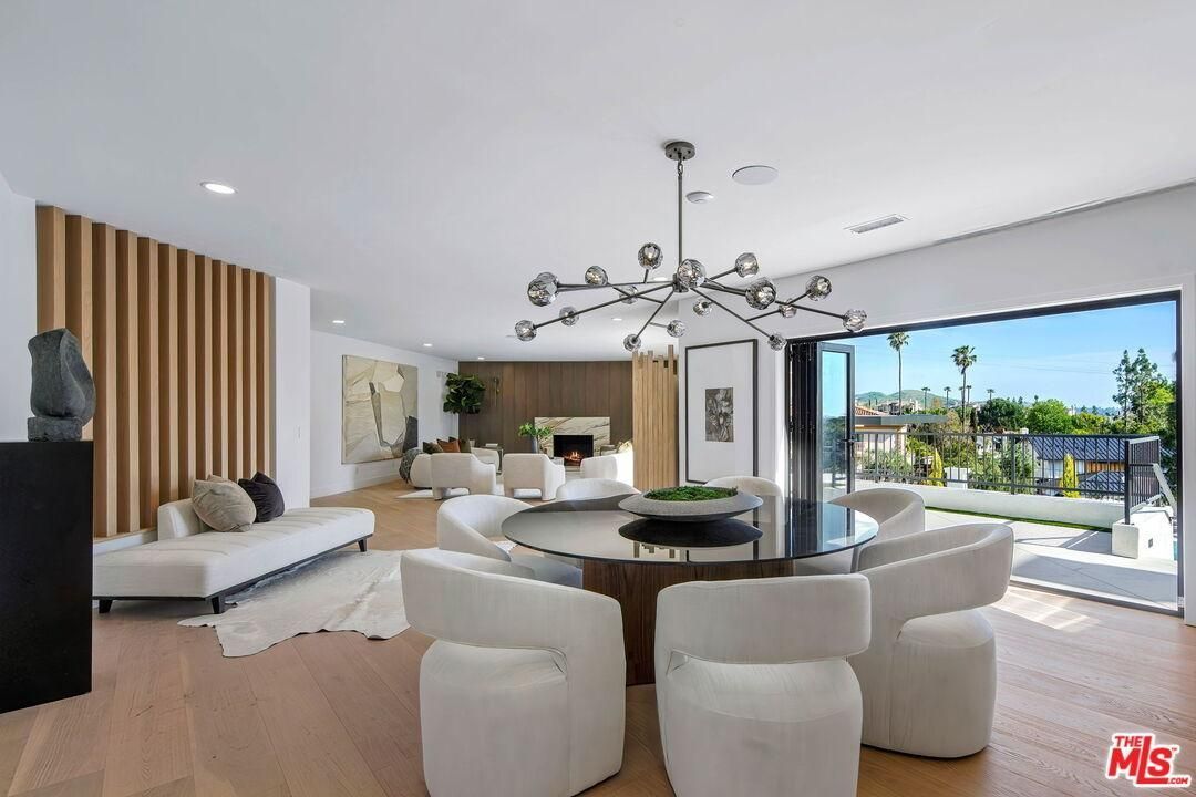Modern open-plan living room with white furniture, wood accents, and large glass doors opening to a pool patio