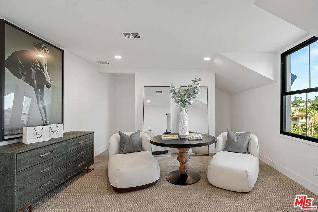 Bright minimalist living room with white seating, round table, dark dresser, and large windows
