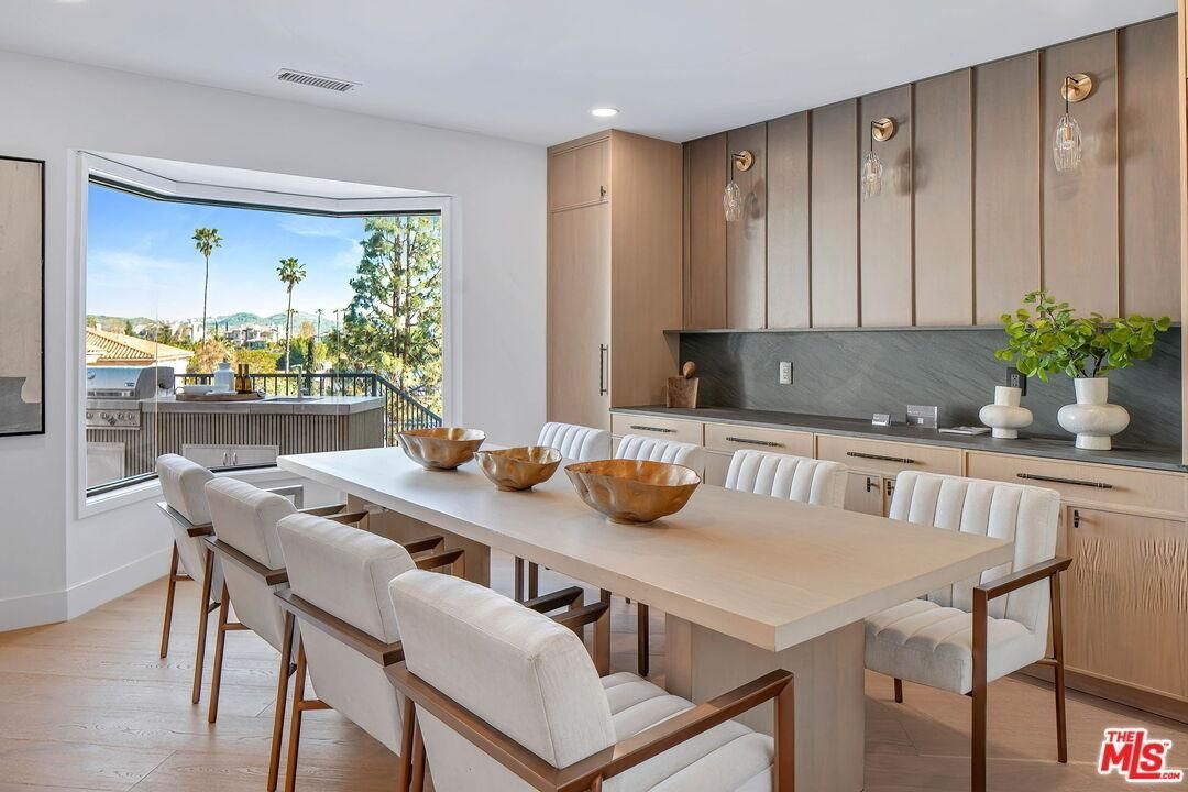 Bright modern dining room with long table, upholstered chairs, wood cabinets, and ocean-view window.