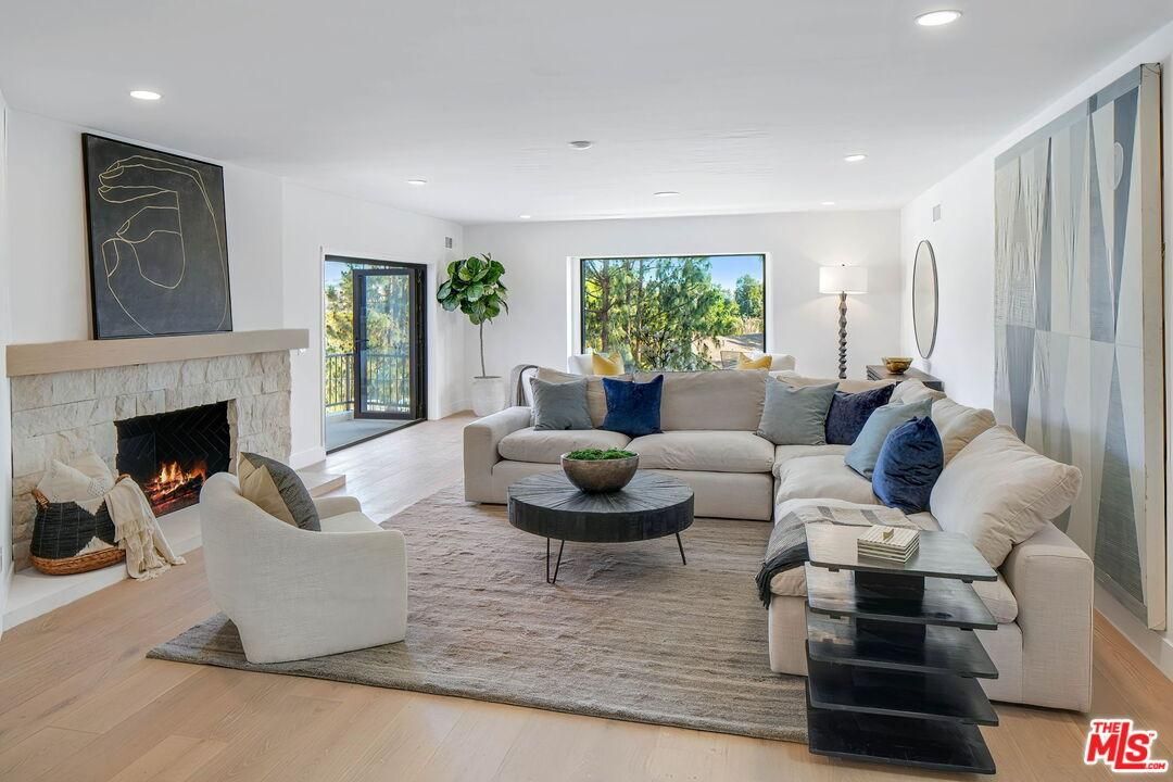 Bright modern living room with fireplace, sectional sofa, blue accents, and large windows overlooking greenery