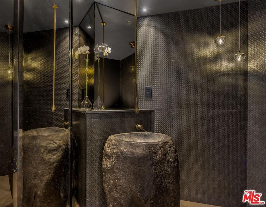Modern dark bathroom with mirror, stone stool, black walls, and warm accent lighting