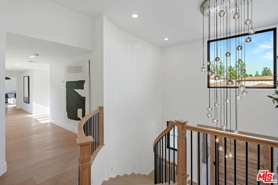 Bright modern staircase landing with wood railings, white paneled walls, and a hanging light fixture near a window.