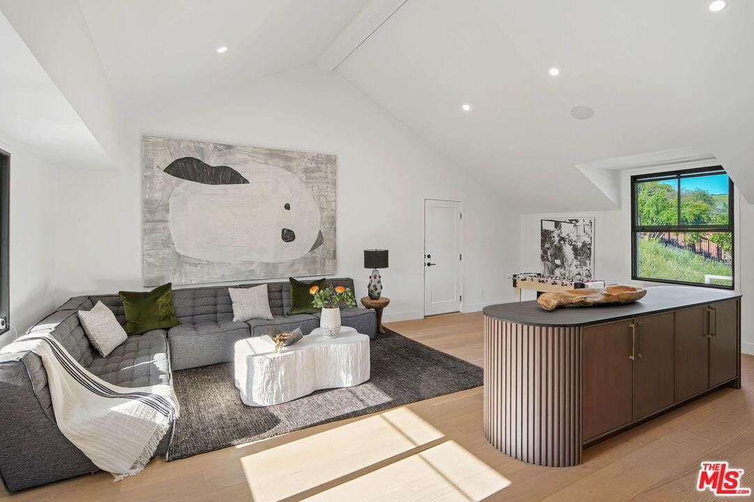 Bright modern living room with gray sectional, island, wall art, and large window overlooking greenery