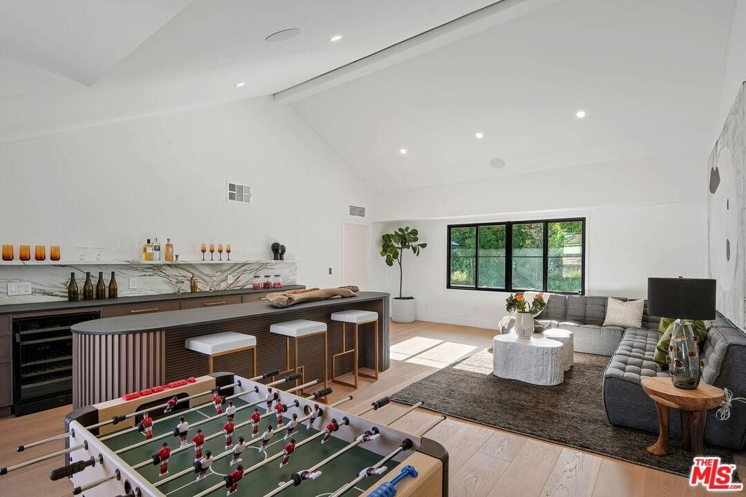 Bright modern open-plan living space with kitchen, sofa, window, and foosball table