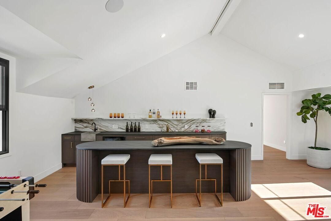 Bright modern kitchen with a large island, bar stools, and white walls in a sunlit open space