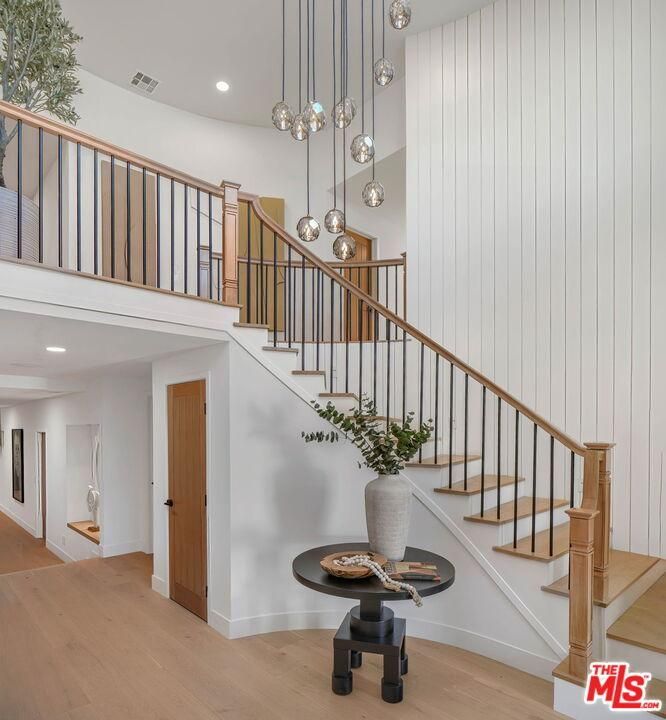 Bright modern foyer with a curved staircase, wood floors, white paneled walls, and hanging pendant lights