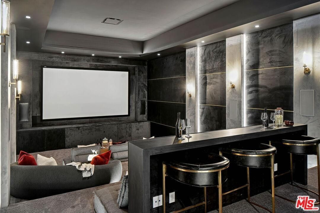Luxury home theater with gray sectional, large screen, dark marble walls, and black bar stools